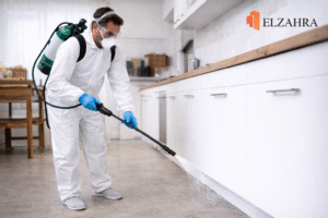 شركة مكافحة حشرات بحي الجامعة – نجران يقوم عامل مختص برش مبيدات مكافحة الحشرات داخل المطبخ باستخدام معدات حديثة مع ظهور شعار ELZAHRA أعلى يمين الصورة
