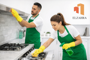 شركة تنظيف بدحضة – نجران عمال تنظيف محترفون يقومون بتنظيف المطابخ بعمق وإزالة الدهون باستخدام معدات حديثة مع وضع شعار الزهراء أعلى الصورة
