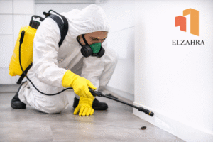 شركة مكافحة حشرات بدحضة – نجران عامل مكافحة حشرات يستخدم معدات رش حديثة للقضاء على الحشرات داخل المنزل مع ظهور شعار الزهراء على الصورة