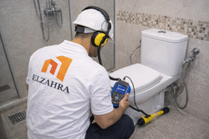 شركة كشف تسربات المياه بدحضة – نجران فني مختص يفحص تسربات المياه داخل الحمام باستخدام أجهزة كشف حديثة مع ظهور شعار الزهراء الرسمي على الزي والصورة