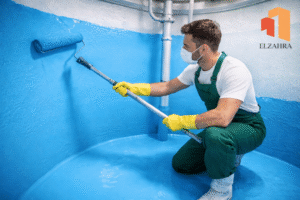 شركة عزل وتنظيف الخزانات بحي الغويلا – نجران عامل يقوم بعزل الخزان من الداخل باستخدام فرشة كبيرة ومادة عزل زرقاء مع ظهور لوجو الزهراء أعلى يمين الصورة